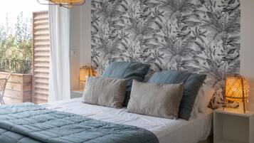 A bedroom with a bed, pillows, a nightstand, a wall with a leaf pattern, and a window with blinds.