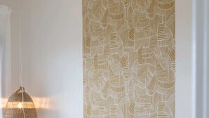 A neatly made bed with a beige quilt, two pillows in mustard and gray, and a patterned wall behind. - T2 Cargese magnificent sea view (Cargèse)