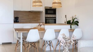 Une cuisine moderne avec des meubles blancs, un plan de travail en bois et un îlot central doté de chaises. Deux luminaires suspendus en osier sont placés au-dessus de l’îlot.