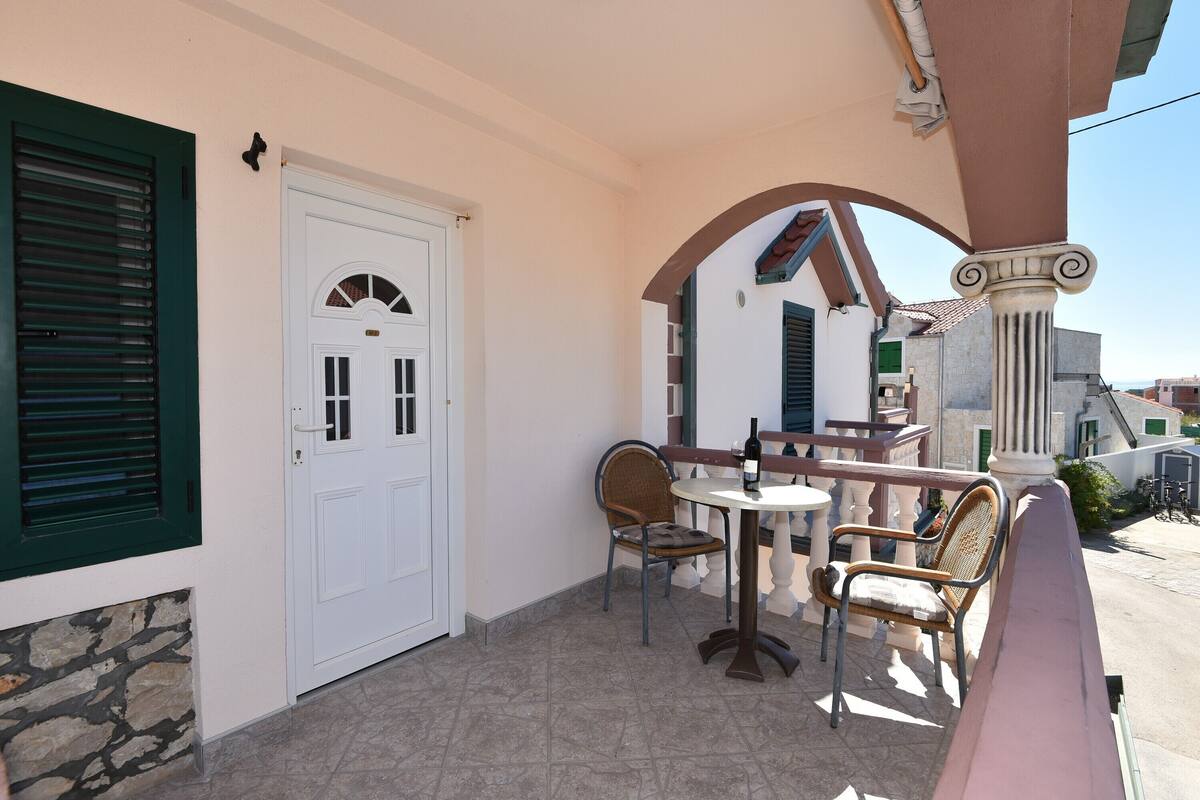 A covered outdoor seating area with a table and two chairs, a white door, and a stone wall.