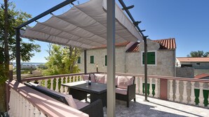 Une terrasse extérieure avec une table et des sièges, un auvent blanc et un bâtiment en pierre en arrière-plan.