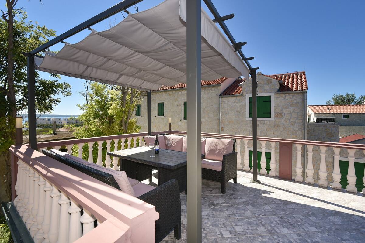 An outdoor patio with a table and seating, a white canopy, and a stone building in the background.