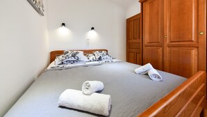 Un lit bien fait, recouvert d’une couvre-lit grise, avec deux lampes fixées au mur et une armoire en bois.