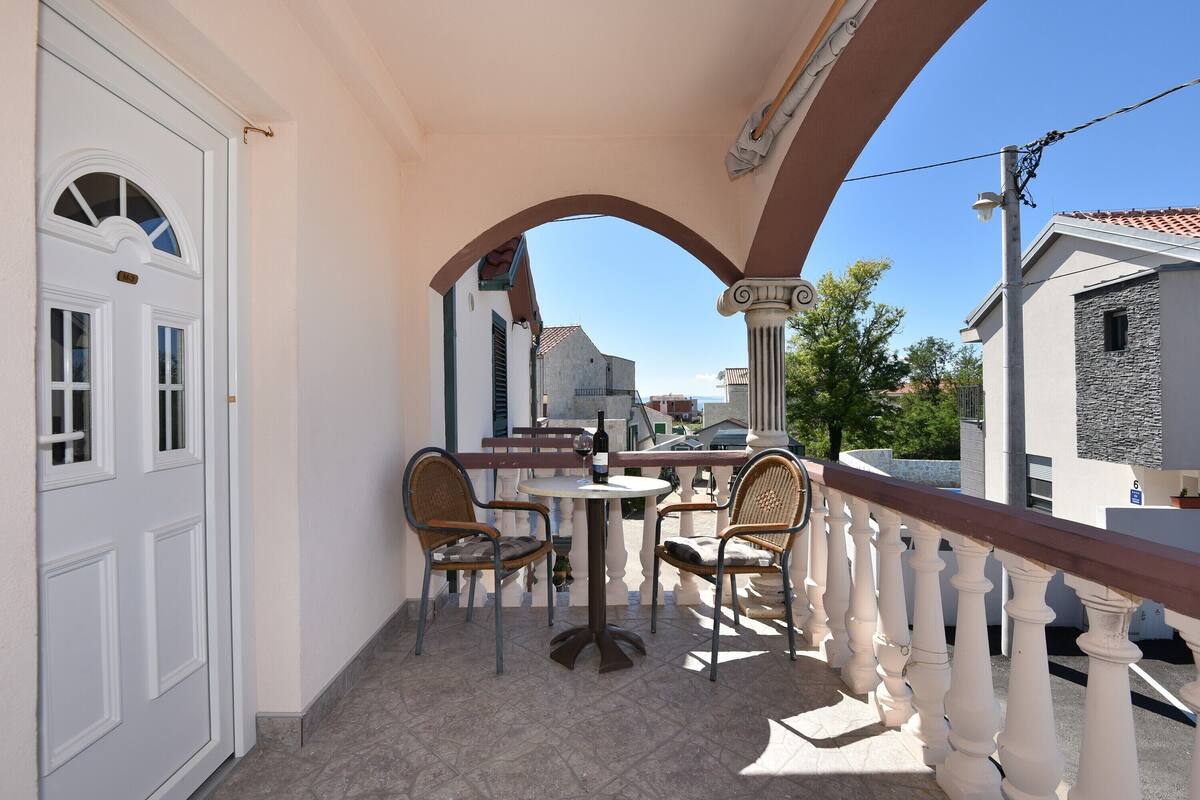 A balcony with a white railing, two wicker chairs, a small round table, and a bottle of wine.