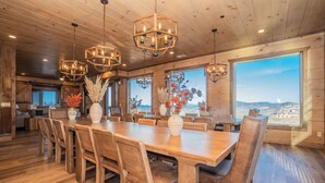 Un vaste espace à manger avec une grande table et des chaises en bois, entouré de grandes fenêtres offrant une vue sur le paysage.