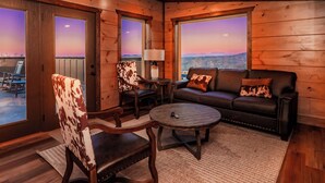 L’intérieur chaleureux d’un chalet comprend un canapé, des fauteuils et une table basse. De grandes fenêtres offrent une vue imprenable sur le paysage.