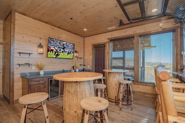 Un intérieur en bois avec un grand téléviseur fixé au mur, des tabourets en bois et un coin bar.