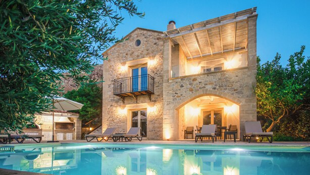 A stone building with a pool, outdoor seating, and a barbecue area.