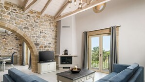 A living room with stone walls, a fireplace, a television, and a large window with curtains.