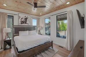 Une chambre avec un plafond en bois, un lit, un ventilateur de plafond et de grandes fenêtres.