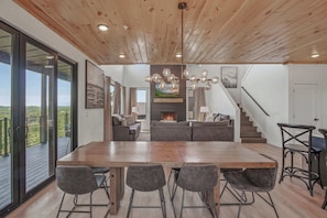 Un vaste espace de vie doté d’un plafond en bois, d’une cheminée, d’une table à manger avec des chaises et d’un escalier.