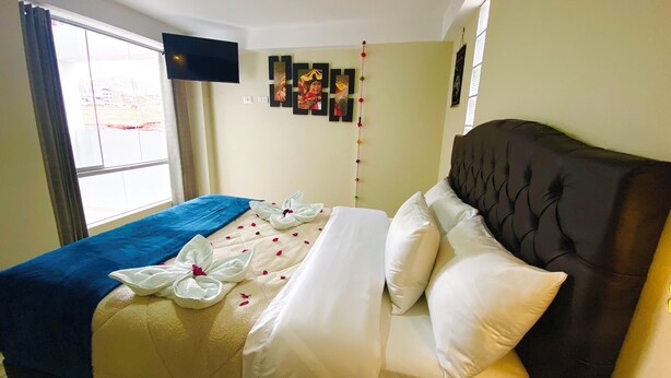 Une chambre d’hôtel avec un lit, un téléviseur fixé au mur et une fenêtre avec des rideaux.