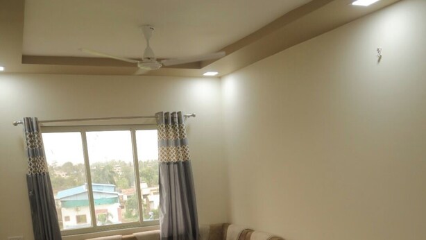 A modern living room with a sectional sofa, a coffee table, and a ceiling fan. - Antique Homestay Daman (Daman)