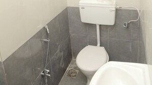 A small bathroom with a toilet, a shower, and a sink. - Antique Homestay Daman (Daman)