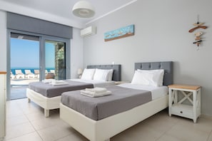 Habitación de hotel con dos camas, un balcón con vistas, una mesita y una obra de arte colgada en la pared.