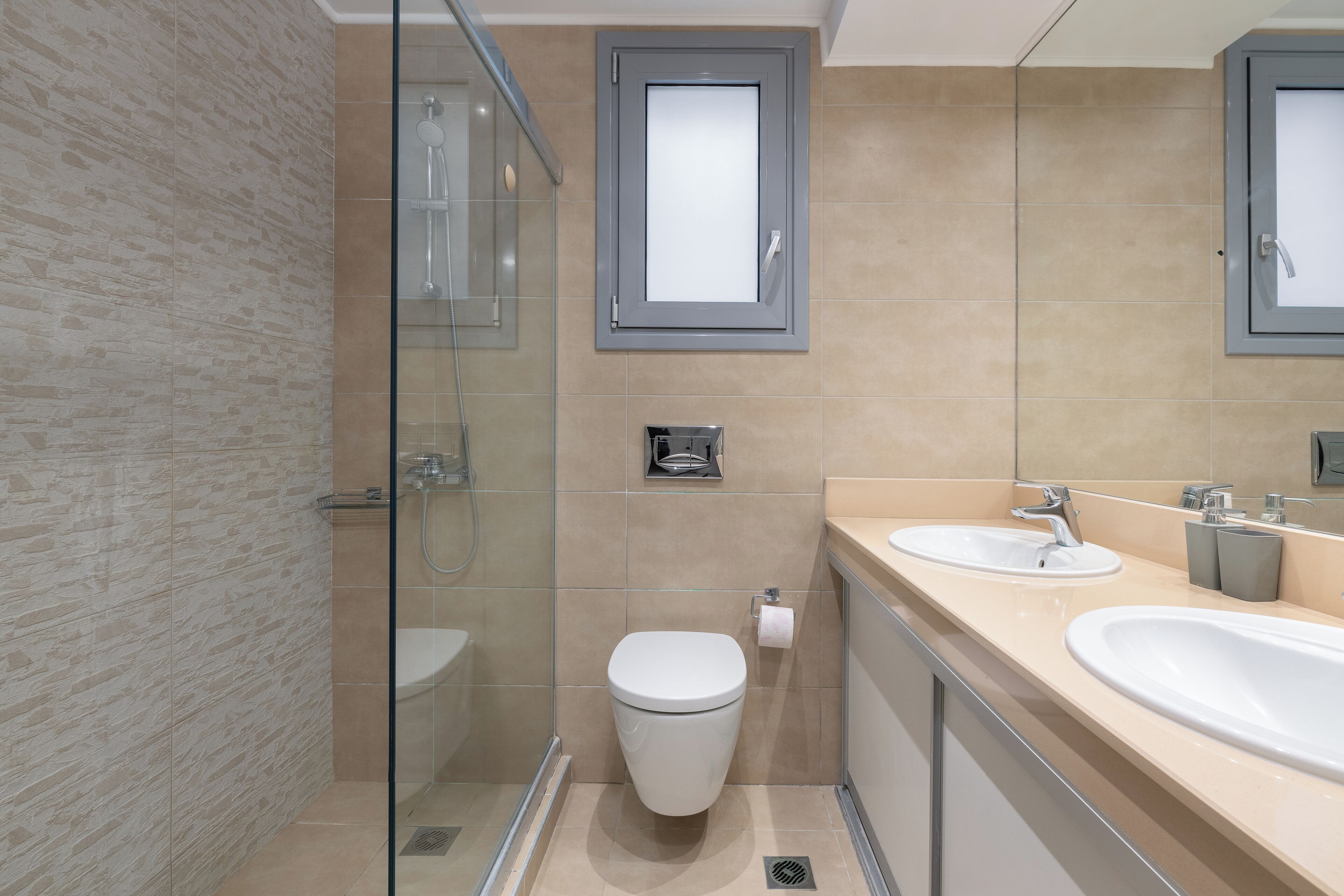 A modern bathroom with a glass shower enclosure, a toilet, and two sinks with mirrors above.