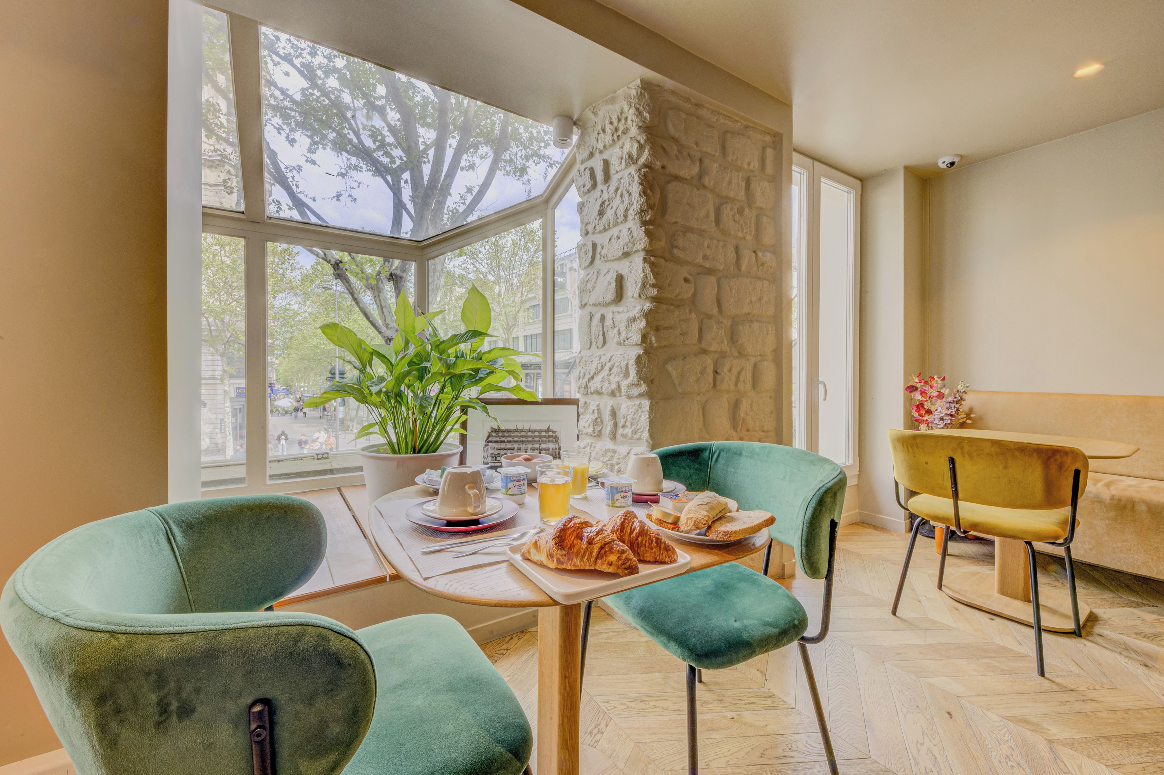 Un comedor con una mesa dispuesta para el desayuno, incluyendo cruasanes y una taza de café, con vista a árboles a través de grandes ventanales.