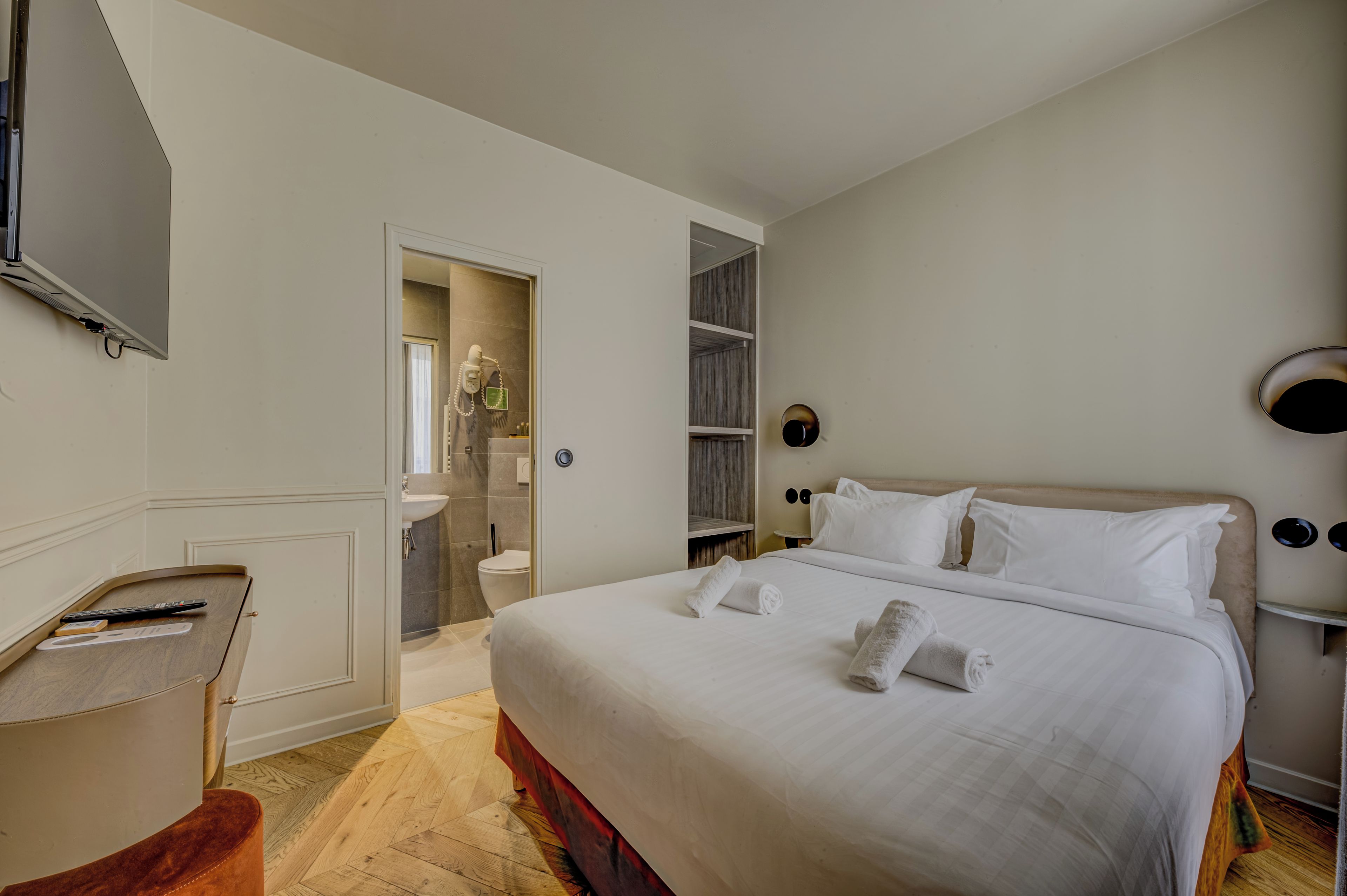 Ein Hotelzimmer mit Bett, Schreibtisch, Spiegel und einem durch eine geöffnete Tür einsehbaren Badezimmer.