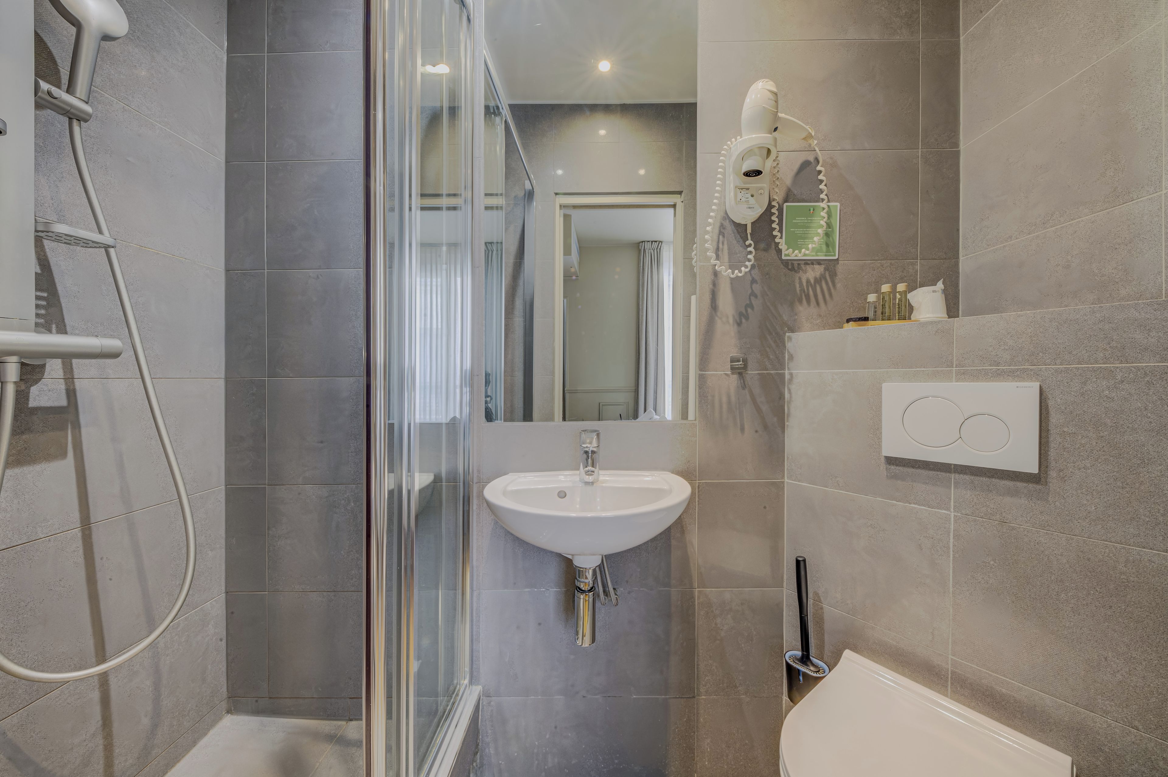 Een moderne badkamer met een douchecabine van glas, een wit wastafeltje en een handdouche.