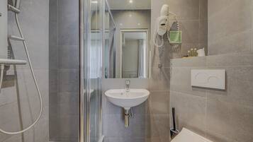 Een moderne badkamer met een douchecabine van glas, een wit wastafeltje en een handdouche.