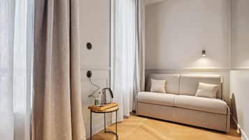 A modern living room with a sofa, a small table with a kettle, and sheer curtains.