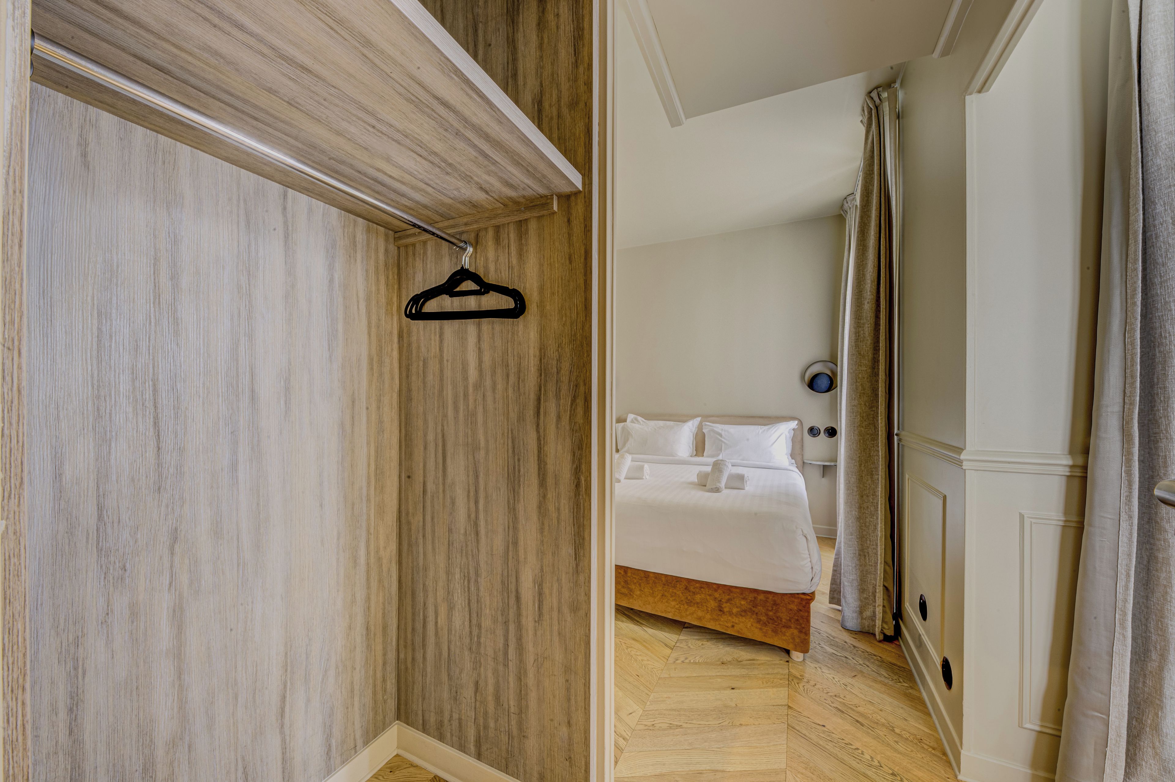 Een hotelkamer met een houten garderobe, een bed met witte lakens en een kapstok.
