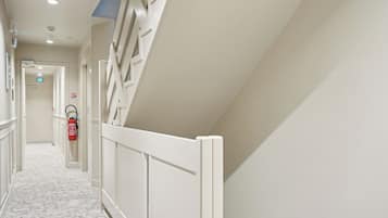 A corridor with white walls, a white railing, and a fire extinguisher on the wall.