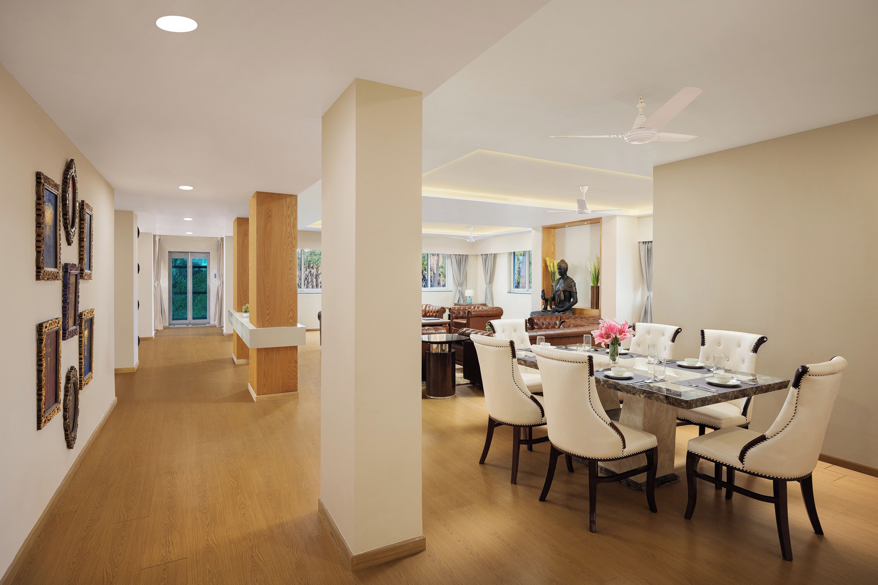 A spacious dining area with a marble table and white upholstered chairs, a wooden floor, and a ceiling fan.