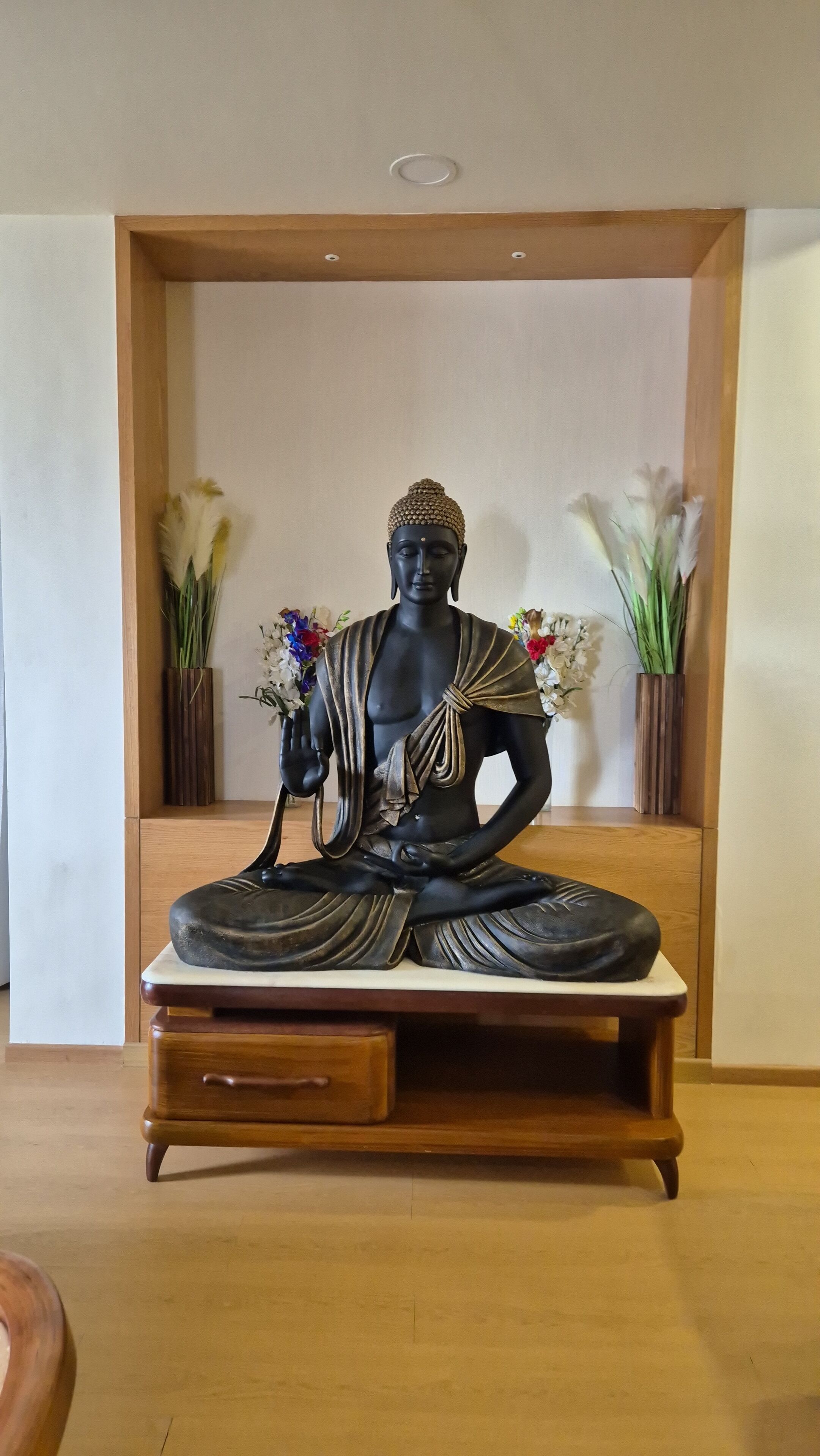 A statue of a seated figure in a meditative pose, placed on a wooden platform with a drawer below.