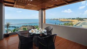 A balcony with wicker chairs and a table, overlooking a coastal view with the sea and a distant landscape. - Ginger Diu Jalandhar Beach (Diu)