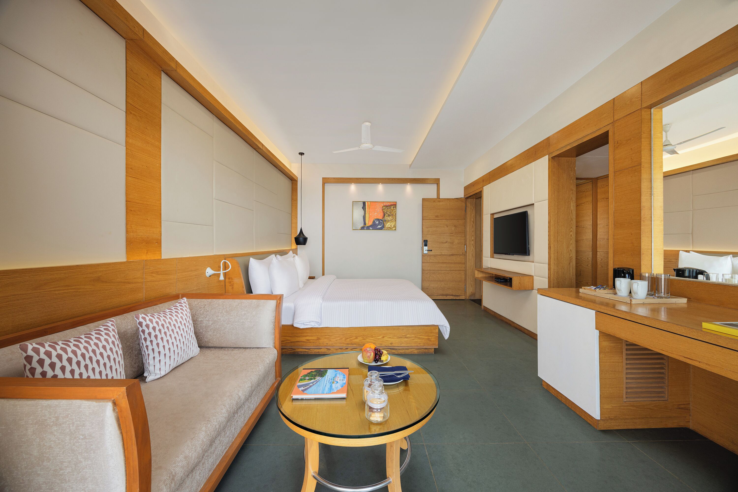 Una habitación de hotel con cama, sofá, una mesita, televisor y espejo.