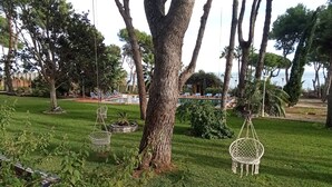 Ein üppiger Garten mit einem großen Baum, Hängestühlen und einem Pool im Hintergrund.