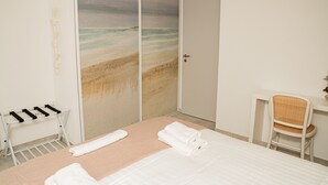 Ein Hotelzimmer mit Bett, Stuhl, Handtuchhalter und einer Tür mit Strandgemälde.