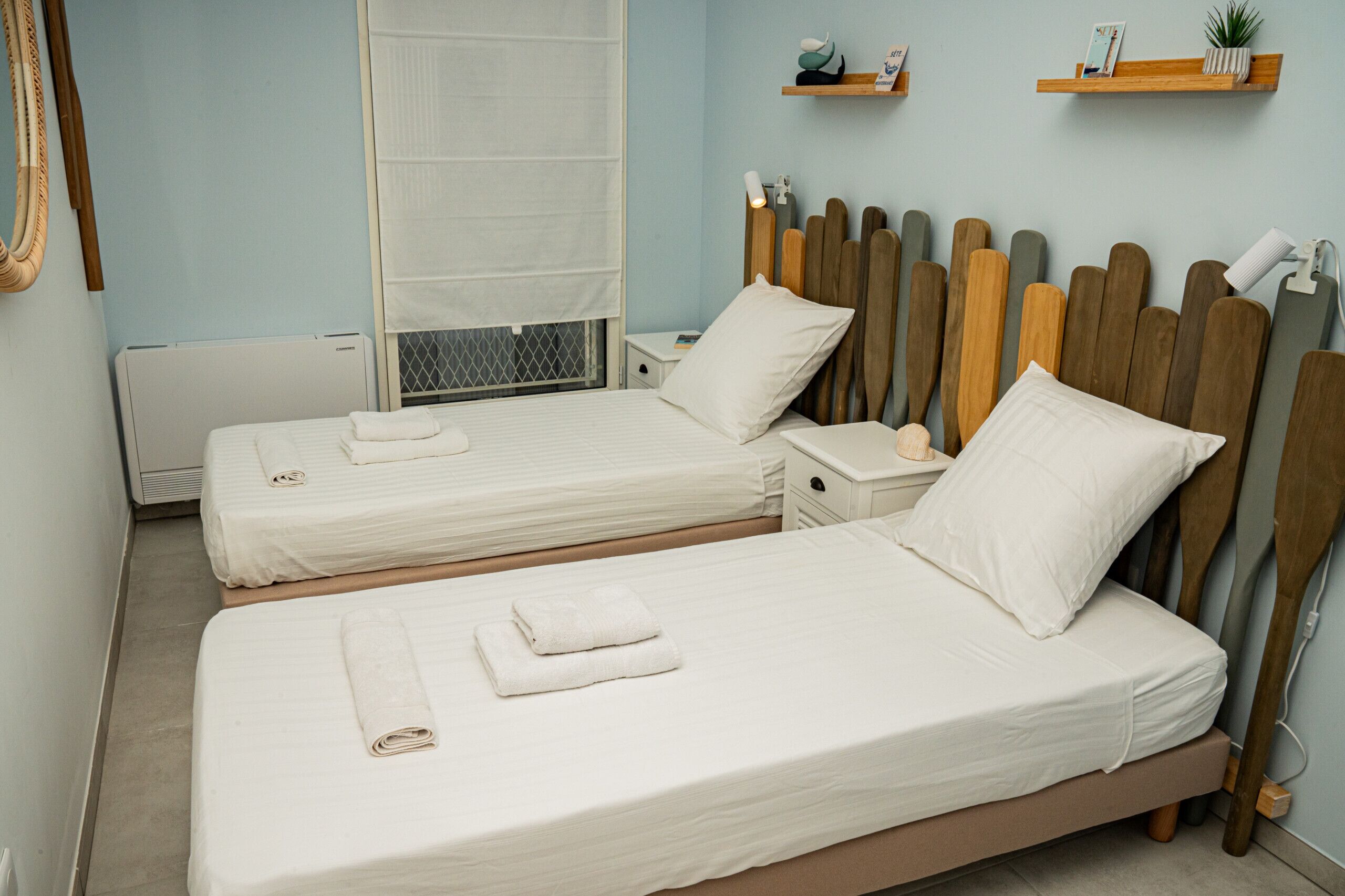 A hotel room with two beds, a wooden headboard, bedside tables, and a window with a white blind.