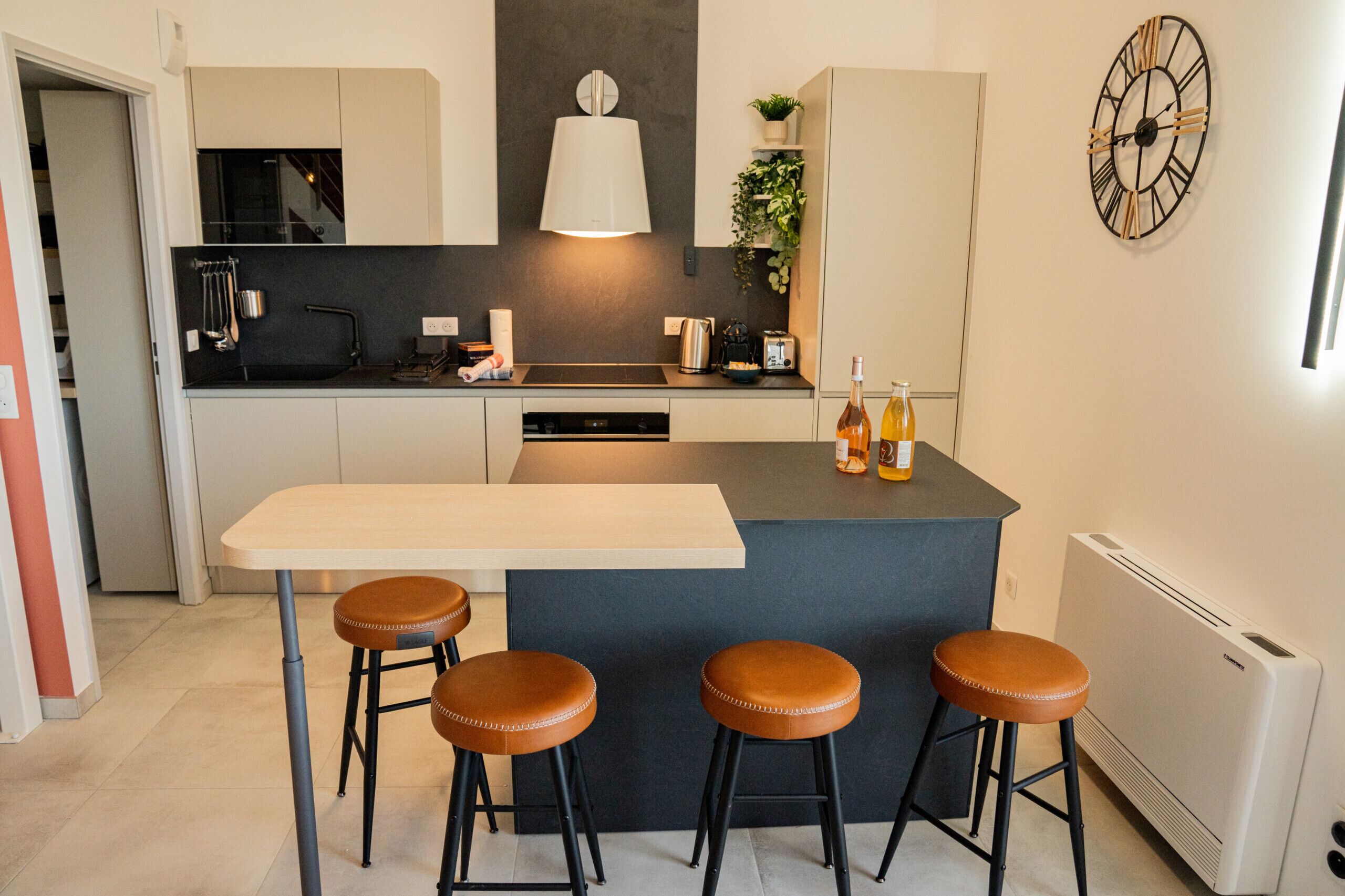 A modern kitchen with a central island, bar stools, and a clock on the wall.