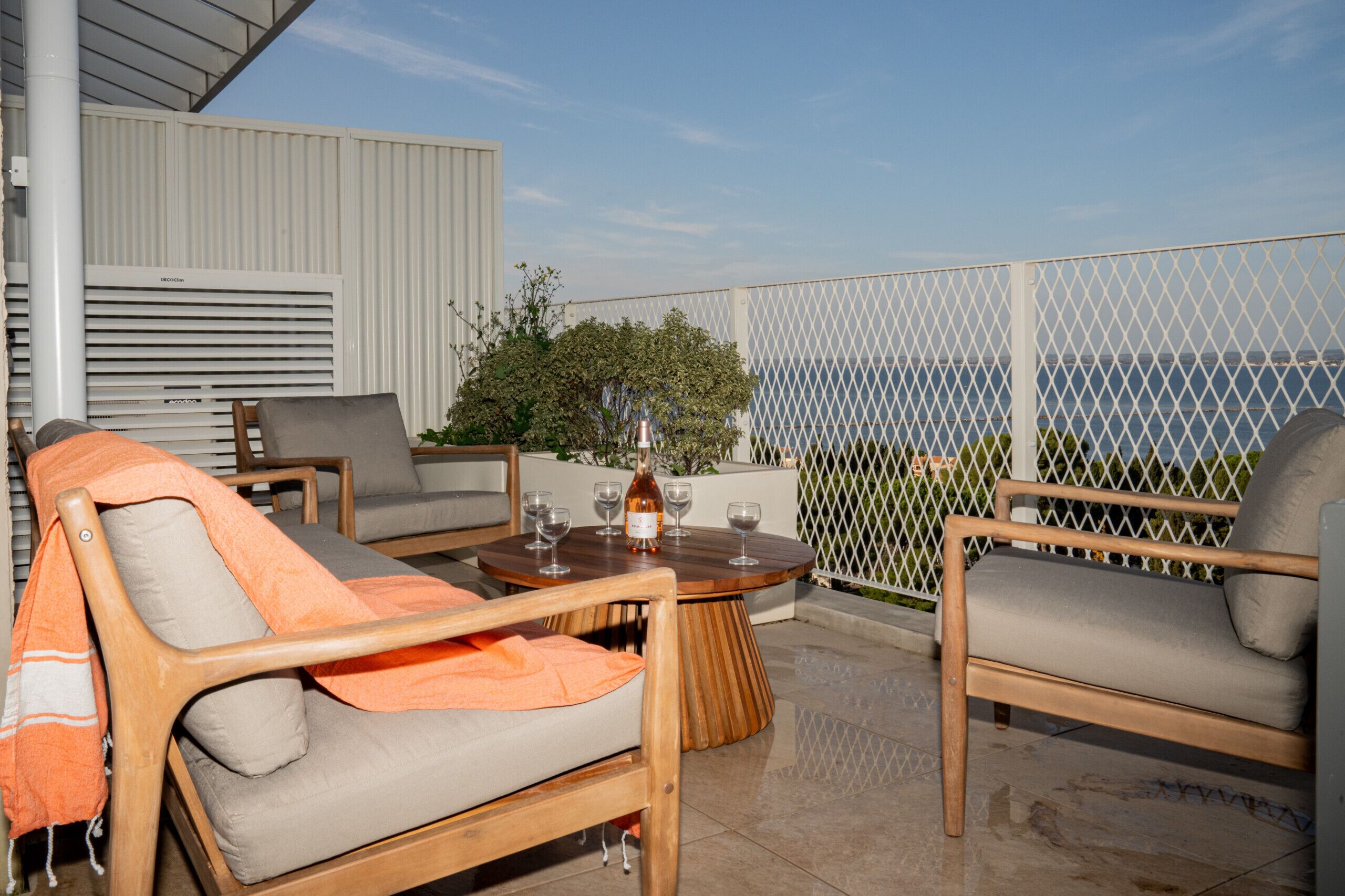 A balcony with two wooden chairs, a small round table with a bottle and glasses, and a view of the sea.