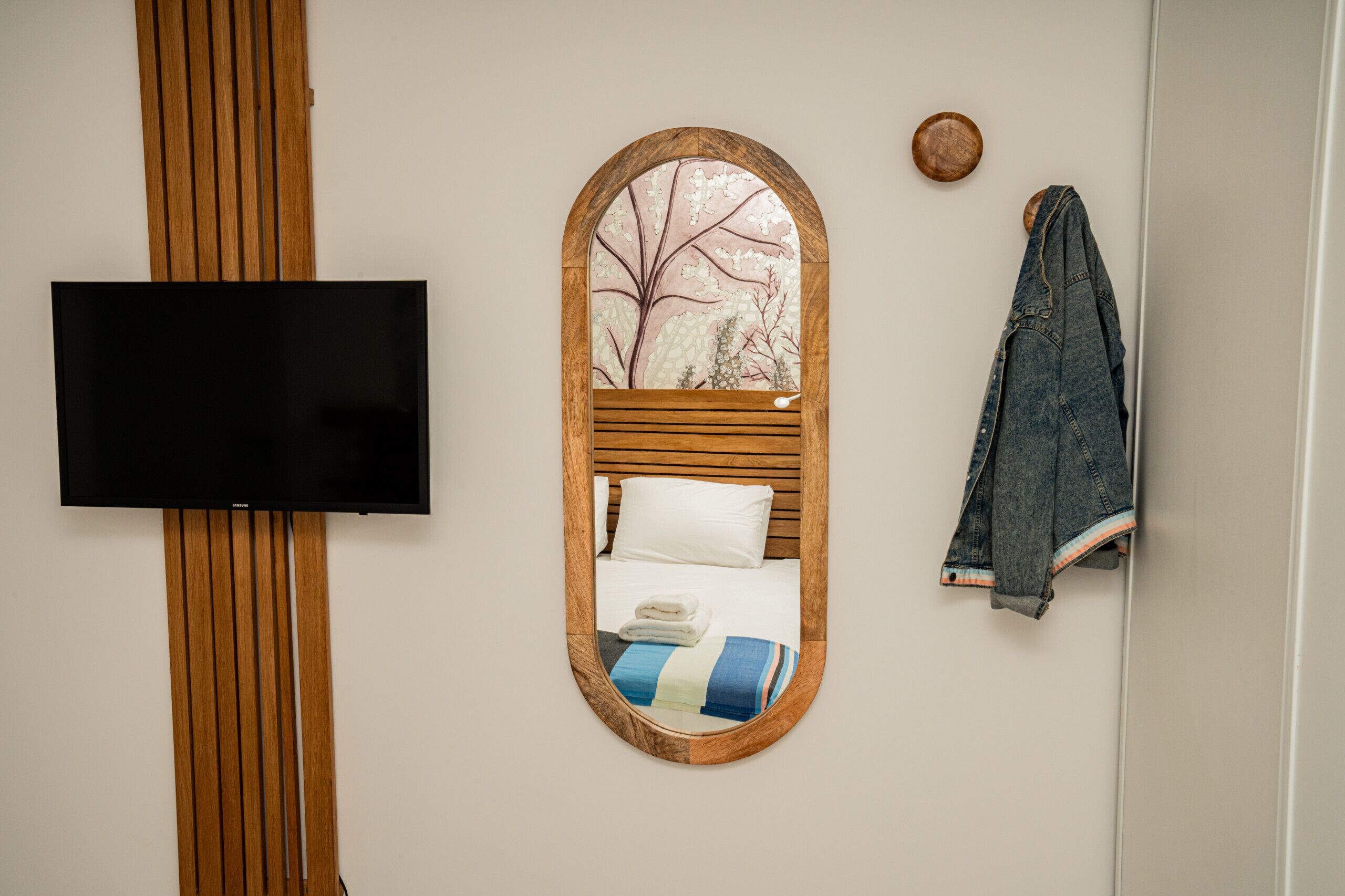 A bedroom with a TV mounted on a wooden panel, a bed with a striped blanket, and a denim jacket hanging on the wall.
