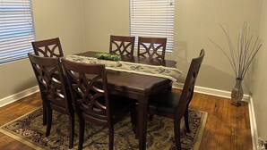 A dining room with a wooden table, four chairs, a small plant, and a vase with sticks. - Spacious 4-Bdrm house in Ruston with WiFi and AC & Wonderful front & back porch (Ruston)