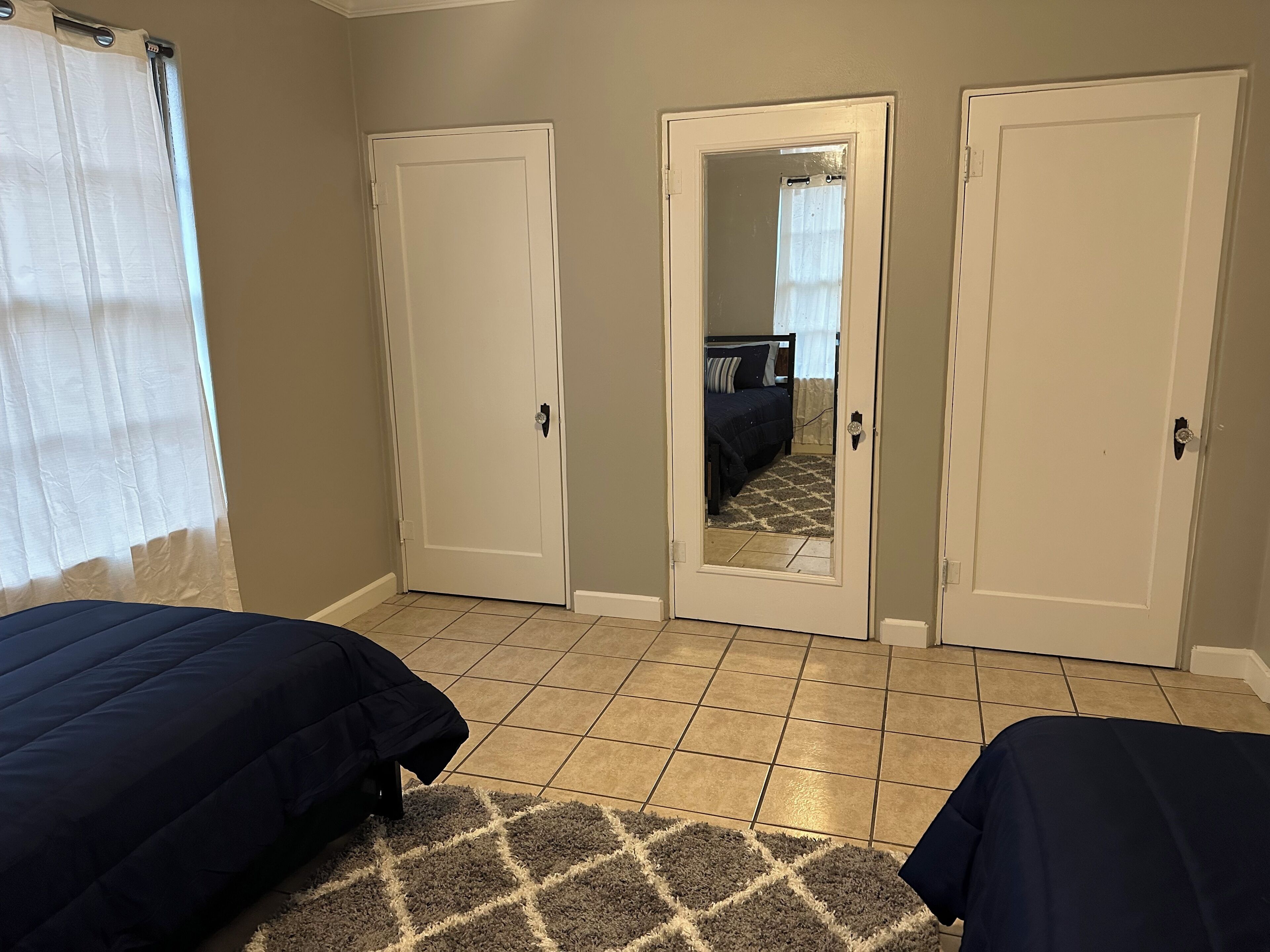 A bedroom with two beds, a large mirror, and a view into another room through a door.