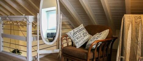 A cozy attic room with a wooden chair, a mirror, and a small table with a glass.