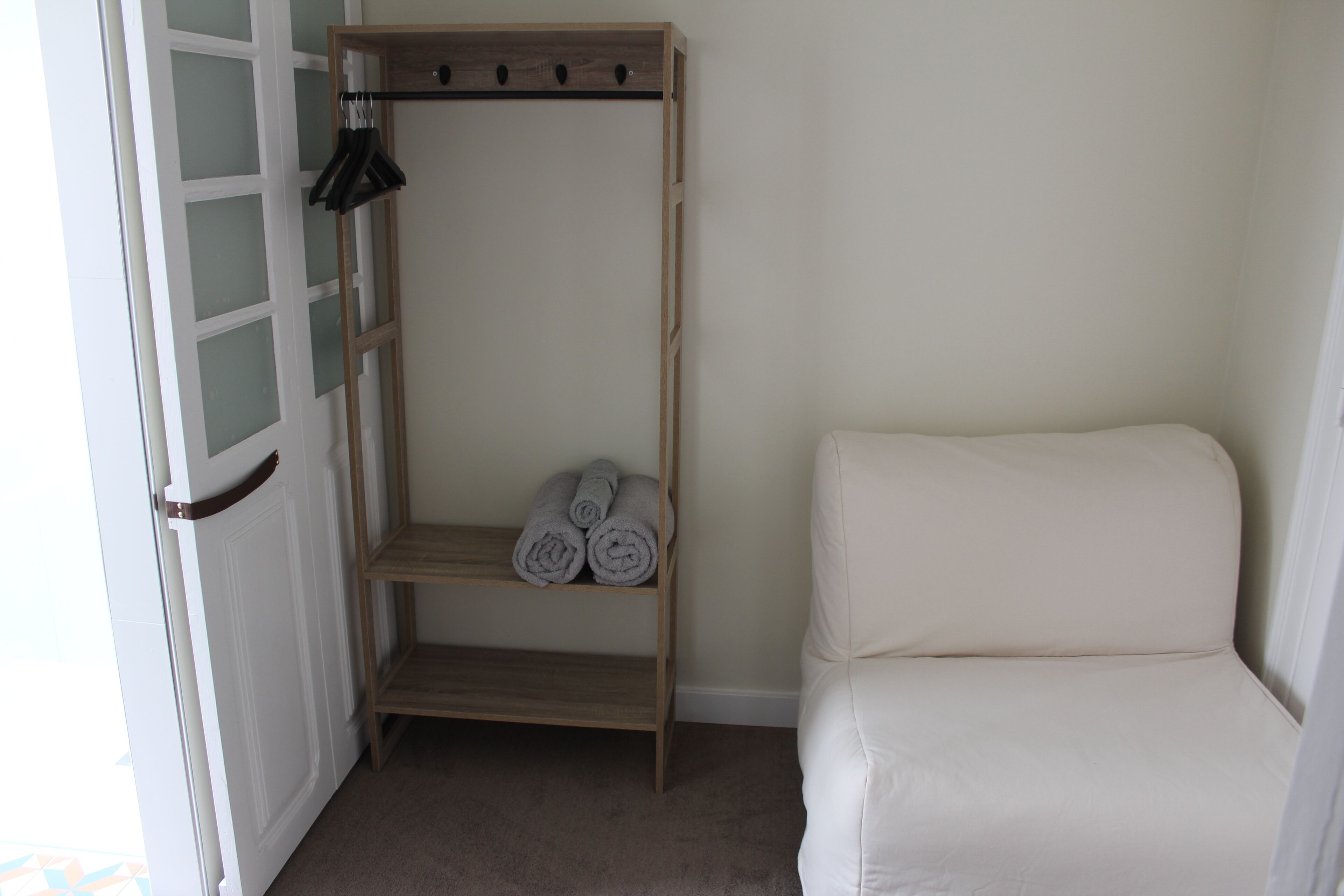 Een kamer met een houten plank met opgerolde handdoeken, een wit kussenbankje en een deur met geëtste glaspanelen.