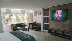 A modern bedroom with a bed, a TV, a sofa, and a desk. - Room 1 of 8 Cozy Suites The Hilltop Guesthouse (Harare)