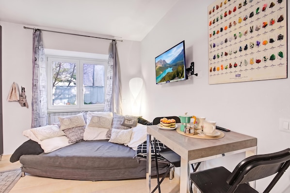 A modern living room with a grey sofa, a flat-screen TV, a dining table with chairs, and a wall-mounted picture of various objects. - Ornavasso Apartments (Ornavasso)