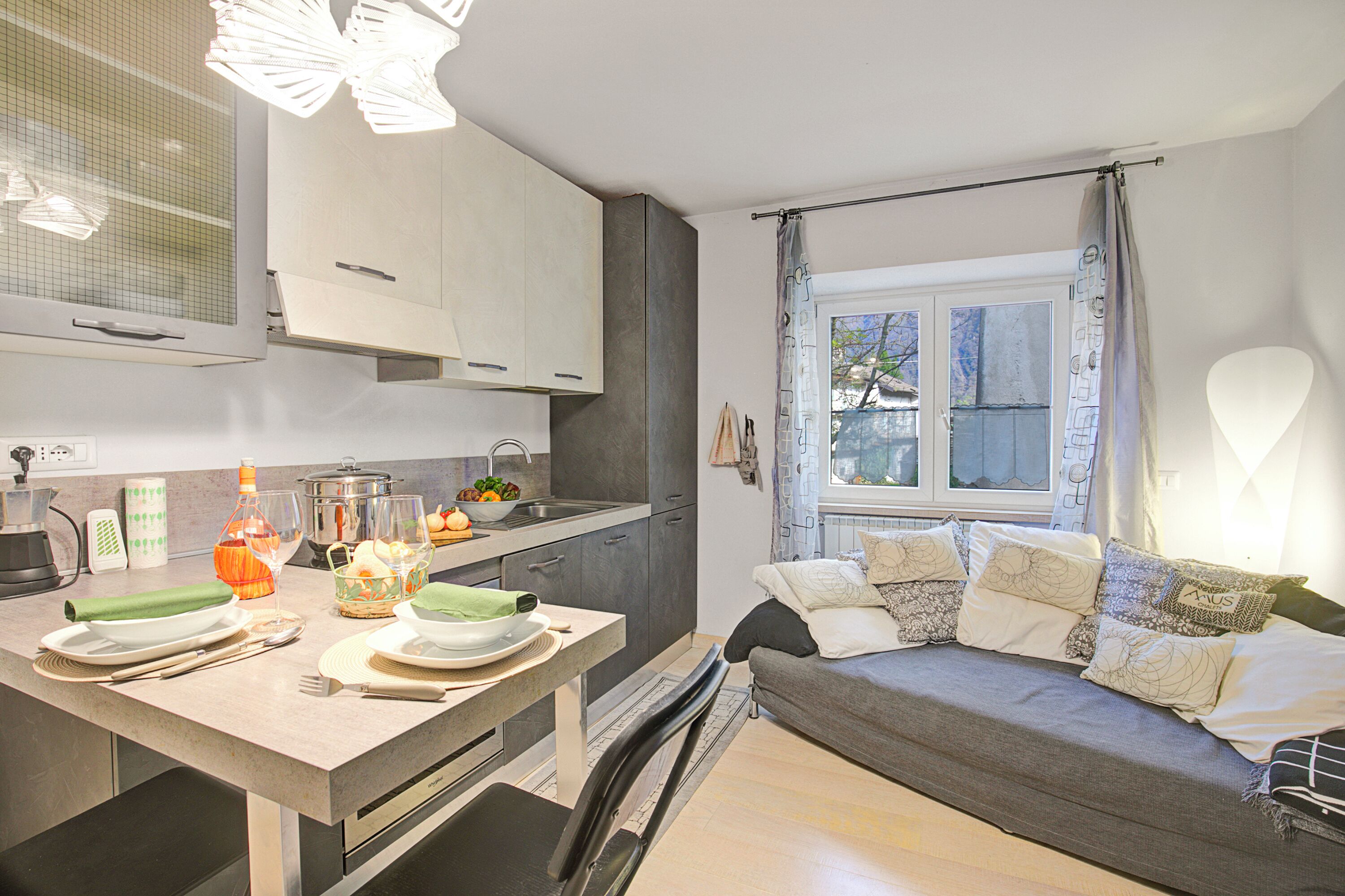 A modern kitchen with a dining area, a sofa, and a window with curtains.