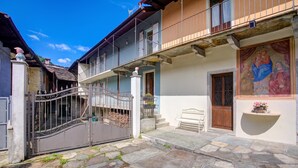A courtyard with stone flooring, a gated entrance, and a building with a balcony and a door with a religious painting. - Ornavasso Apartments (Ornavasso)