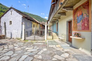 A stone-paved courtyard with a metal gate, a bench, and a building with a balcony. - Ornavasso Apartments (Ornavasso)
