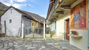 Un patio empedrado con una verja de metal, una pequeña silla blanca y un edificio con un balcón y un cuadro religioso.