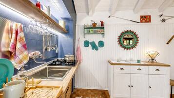 A kitchen with a stove, sink, and various utensils. There are cabinets, a mirror, and a shelf with decorative items.