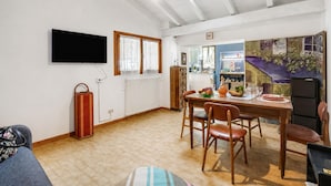 Et spiseområde med et bord dækket til fire personer, et fjernsyn ophængt på væggen og en radiator.