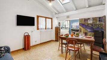 A dining area with a table set for four, a television mounted on the wall, and a radiator on the wall.